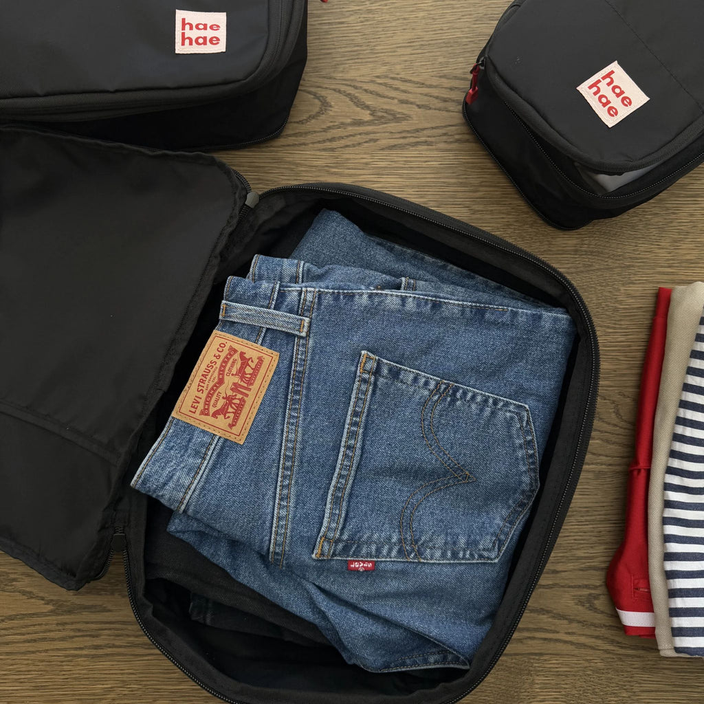 Folded blue jeans in a black compression packing cube with hae hae branding on a wooden surface.