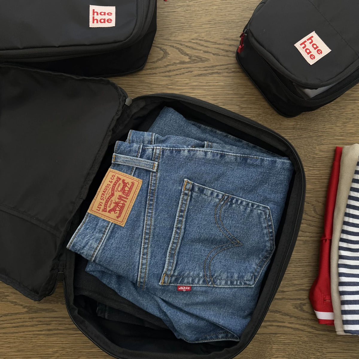 Folded blue jeans in a black compression packing cube with hae hae branding on a wooden surface.
