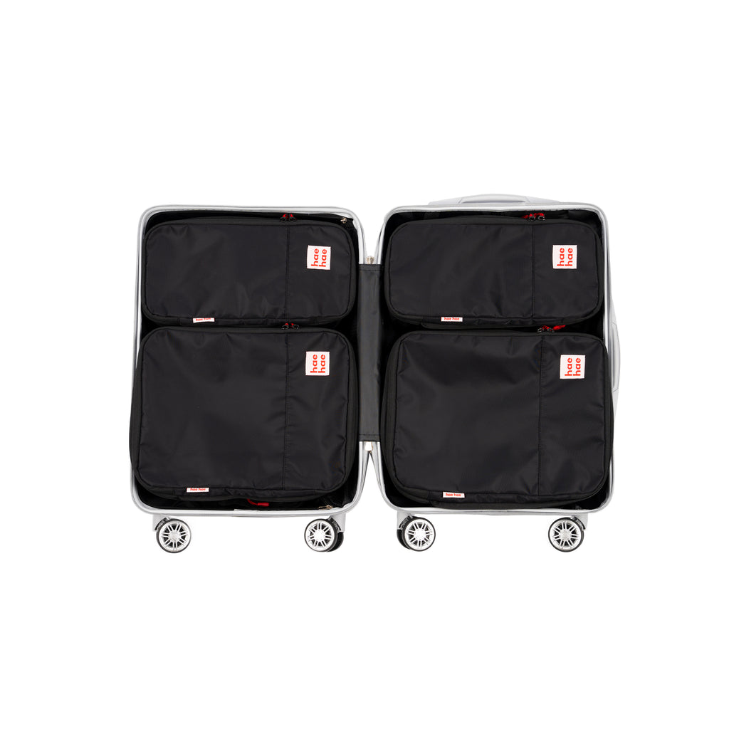 Four black hae hae packing cubes with small red-and-pink brand tags, arranged inside an open light gray suitcase on a white background.
