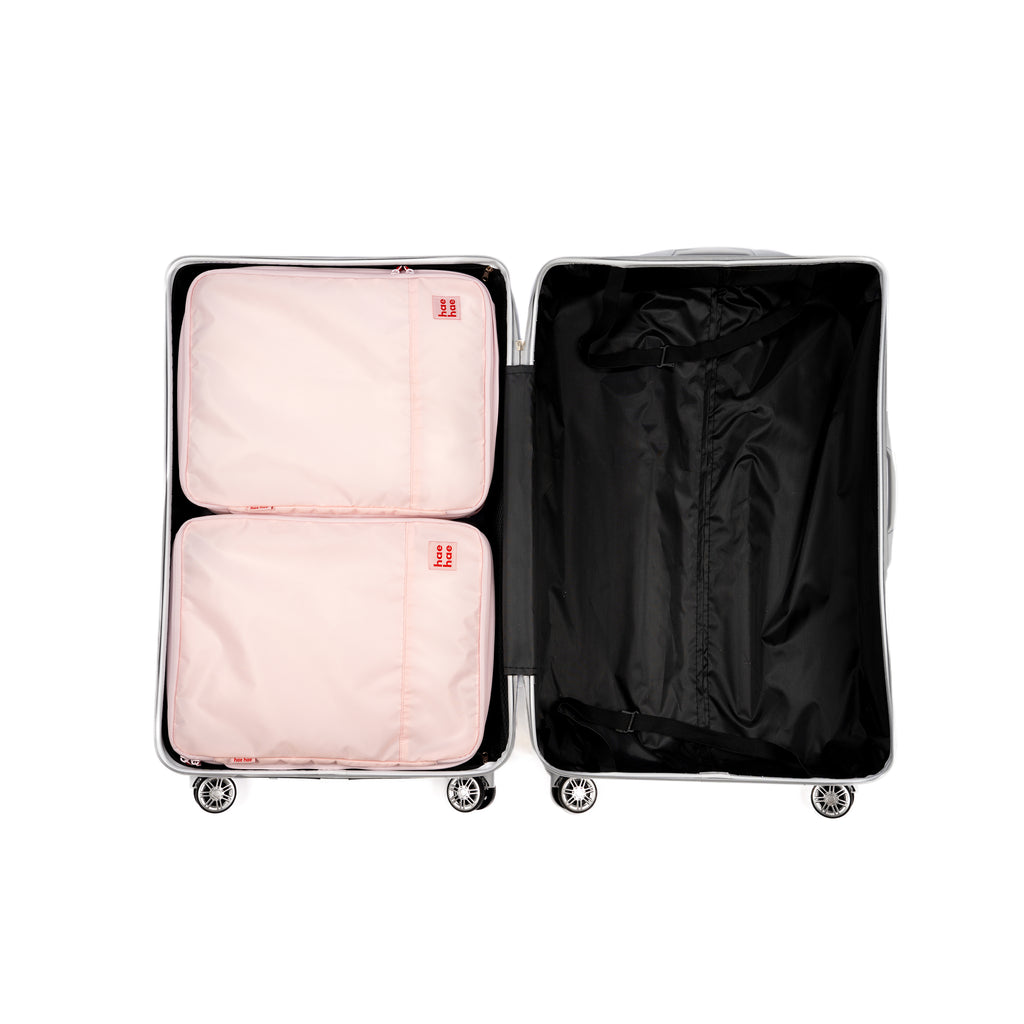 Open suitcase with pink packing cubes and a black garment inside on a white background