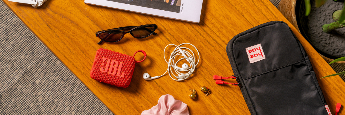 JBL speaker, sunglasses, earbuds, and a black hae hae packing cube in small on a wooden surface.